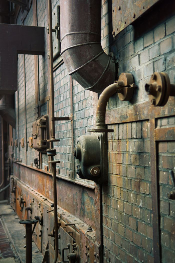 Explore the intricate details of a vintage factory wall featuring pipes and rusted metal elements.